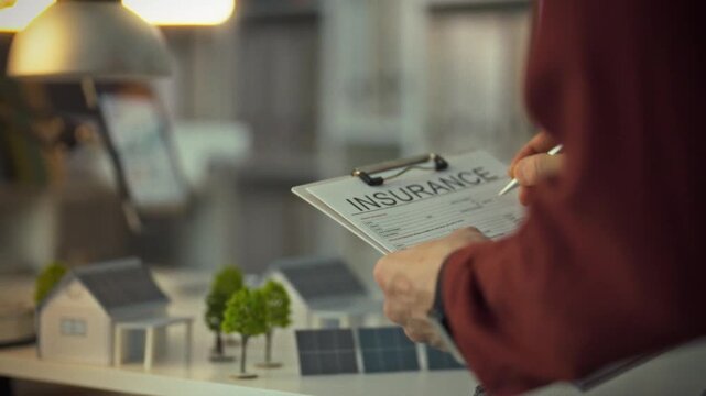 A person is examining an insurance form at a workspace filled with models of houses and solar panels. The scene showcases planning for a sustainable housing initiative