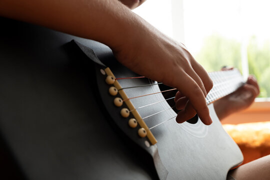 Close-up of hands playing an acoustic guitar, pressing strings and strumming near the fretboard. - Powered by Adobe