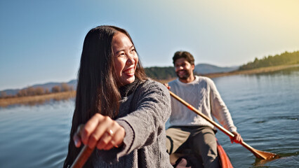 Fototapeta premium A smiling Asian woman paddles a canoe on a serene lake, with a man rowing behind her. They enjoy a peaceful weekend activity, embracing an active lifestyle together.
