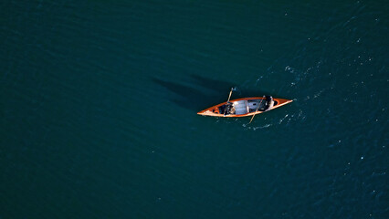 Fototapeta premium A couple paddles a canoe on a serene, deep blue lake, embodying a weekend escape into nature. The tranquil setting, captured with an aerial shot, highlights their active lifestyle and connection.