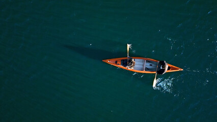 A couple paddles an orange canoe on a serene, turquoise lake, embodying a weekend escape into nature. The image captures their synchronized effort, highlighting teamwork and the joy.