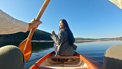 A young woman paddles a canoe on a serene lake, her long hair flowing. A hand reaches out to hold...