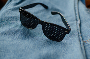 Black pinhole glasses designed for vision correction and eye exercises sitting on denim