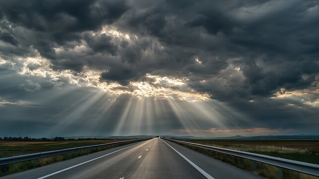 Dramatic sun rays breaking through dark storm clouds over an empty highway