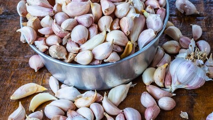 Abundant fresh garlic cloves piled in a metal bowl on a wooden surface