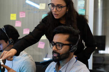 Customer support team in a modern call center receiving guidance from a supervisor. Diverse employees working with headsets and computers, representing teamwork, communication, and business
