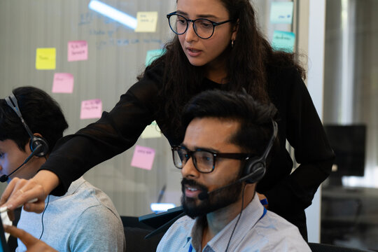 Customer support team in a modern call center receiving guidance from a supervisor. Diverse employees working with headsets and computers, representing teamwork, communication, and business 