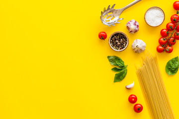 Flat lay of uncooked spaghetti with ingredients for cooking Italian pasta - tomatoes and basil with garlic - on a yellow background, top view