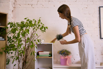 Young woman organizing home shelf and placing decor plant. Concept of tidy lifestyle, calm home...