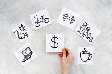 Hand is choosing Dollar card from many paper cards with hand drawing of different life activities. Life balance concept.