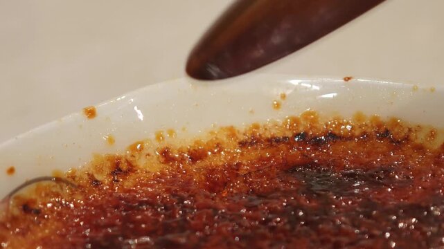 Spoon cracking creme brulee caramel crust and scooping custard close up