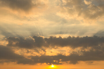 Sunbeams break dramatically through dense clouds in the orange sky.