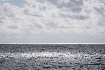 Calm ocean waves reflect sunlight under a cloudy sky on a peaceful day at the beach, creating a serene atmosphere and inviting relaxation
