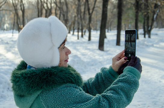 Senior woman holding your smartphone at arms length in a snowy park, photographing landscape and taking selfies - Powered by Adobe