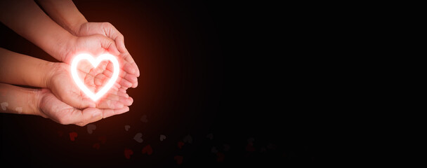 Bright neon heart resting in overlapping hands representing love and care, health care, CSR, insurance, family, World Heart Day, World Health Day, love, rescue, wellbeing, hope, support, compassion