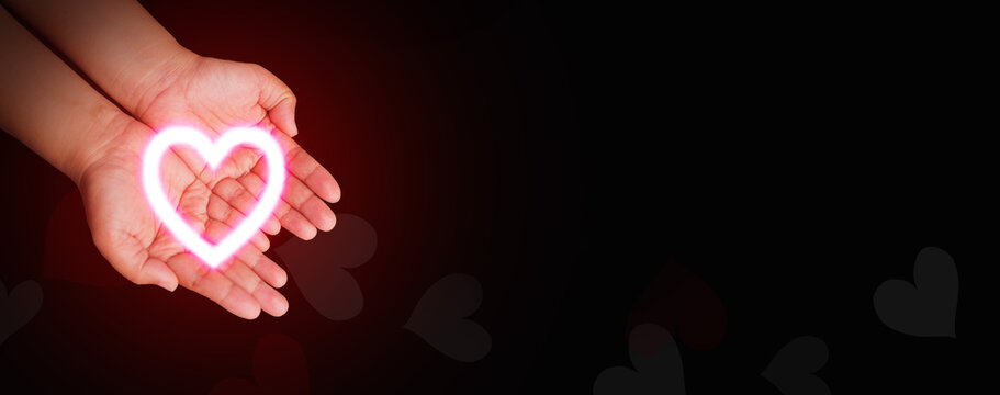Hands gently holding a glowing heart shape against a dark background. Health care, CSR, insurance, family, World Heart Day, World Health Day, love, rescue, wellbeing, hope, support, and compassion