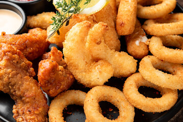 A close-up, appetizing shot of a golden-brown assorted fried seafood and appetizer platter, featuring crispy shrimp, calamari rings, and mozzarella sticks with dipping sauces