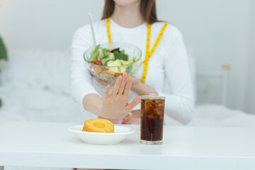 Woman holding healthy salad while refusing soda and donut, representing clean eating, healthy diet choices and weight management at home. Concept of nutrition awareness and fitness lifestyle.
