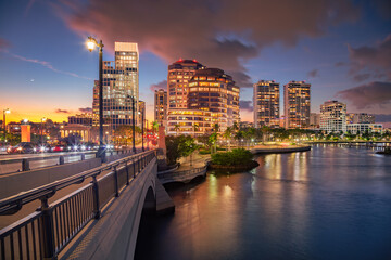 West Palm Beach, Florida, USA. Cityscape image of West Palm Beach, Florida with bridge leading to the downtown and reflection of the city skyline in the water at beautiful sunset.