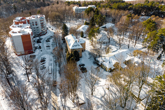 Aerial view of resort buildings nestled in a snowy, wintry forest landscape with bare trees and bright sunshine