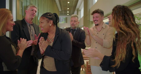 Happy woman smiling as diverse team applauds in corporate hallway, professionals expressing encouragement and unity in workplace setting