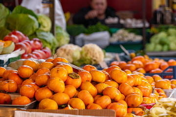 A view of a pile of persimmons on display at a local farmers' market. Persimmons in a farmer's market display, sold at the supermarket produce counter, showcase organic, vegetarian, and healthy foods.