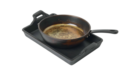 Dirty skillet sits on a grey griddle, grease present