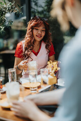 A stylish woman with red hair in a pink vest enjoys a sunny outdoor cafe moment, pouring a coffee drink for a friend. The scene features drinks, glasses, and a warm, relaxed atmosphere.