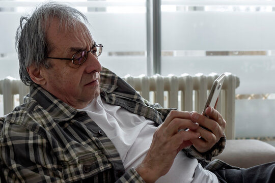 Senior man, happy and phone on couch for texting, reading or thinking for contact in home living room. Elderly person, smartphone and smile for notification, social media app and relax on lounge sofa