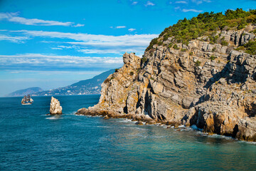 Fototapeta premium Rocky coast by the blue sea with an island of rock on a clear sunny day. Landscape, sights of Russia, sea, mountains.