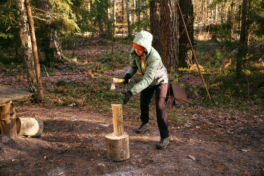A young woman is chopping wood with an axe in the forest. The concept of preparing firewood for the winter stove. - Powered by Adobe