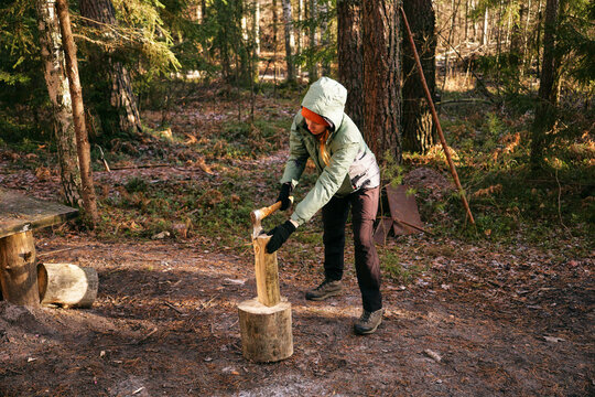 A young woman is chopping wood with an axe in the forest. The concept of preparing firewood for the winter stove.