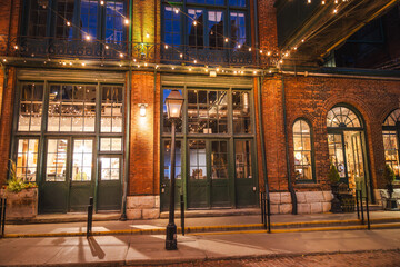 Fototapeta premium Historic brick storefronts illuminated by warm lights in the Distillery District of Toronto during the evening.