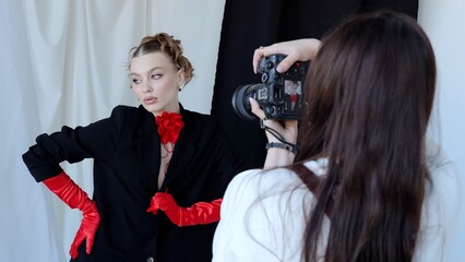 Fashion photographer taking pictures of a beautiful model wearing red gloves and a red flower choker, posing in a studio with black and white background