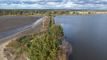 Obraz premium Aerial contrast between dried and full lake in rural Poland. Aerial view of a narrow land strip separating a dried reservoir from a full lake, surrounded by forest and farmland in rural Poland