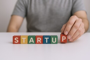 Hand arranging wooden blocks spelling startup on white table, concept for beginning new business
