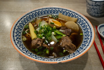 Close-up of authentic Taiwanese Beef Noodle Soup with tender beef chunks, white radish, baby corn, and half a boiled egg in a traditional patterned bowl.