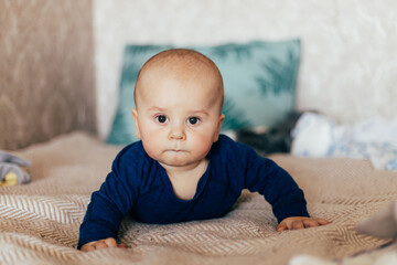A cute baby lying on their stomach on a bed, looking forward with a curious expression. Warm natural light and a cozy home environment create a tender and intimate family scene.