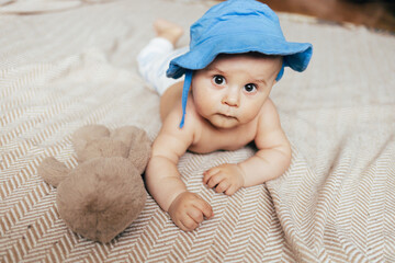 A baby lying on their stomach on a soft blanket reaches for colorful toys in a play area. Warm natural light and a cozy home environment create a bright and engaging family moment.