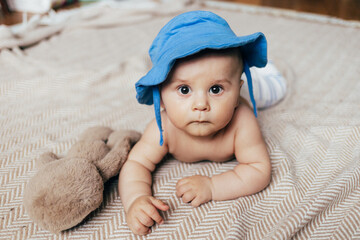 A baby lying on their stomach on a soft blanket reaches for colorful toys in a play area. Warm natural light and a cozy home environment create a bright and engaging family moment.