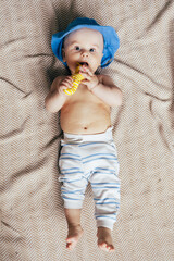 A baby lying on their stomach on a soft blanket reaches for colorful toys in a play area. Warm natural light and a cozy home environment create a bright and engaging family moment.
