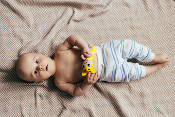 A baby lying on their stomach on a soft blanket reaches for colorful toys in a play area. Warm natural light and a cozy home environment create a bright and engaging family moment.
