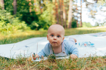 The photo shows a baby lying on a soft star-patterned cushion outdoors. The child is looking directly at the camera while sucking on a pacifier. The warm sunlight and green background create a peacefu
