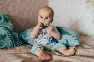 A cute baby lying on their stomach on a bed, looking forward with a curious expression. Warm natural light and a cozy home environment create a tender and intimate family scene.