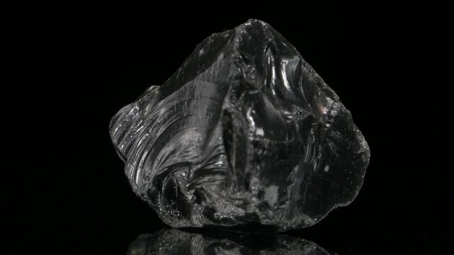 Obsidian - black silica-rich volcanic glass formed by rapidly-cooled viscous lava - revolving slowly against a black background