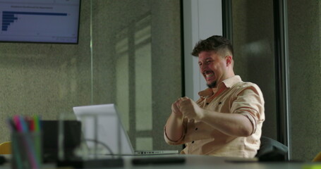 Happy young man celebrates success alone at laptop with double fist pump during solo office work...