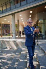 Senior man using smartphone on modern building stairs