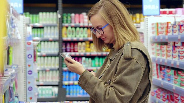 Young woman browsing supermarket aisles, comparing different toothpaste brands. Evaluating options for her oral care routine while selecting products