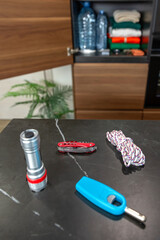 Survival kit on kitchen counter with multitool knife, lighter, flashlight and rope. 72 hour emergency supplies stored in pantry closet on background. Alert, foresight and self sufficiency strategy.