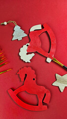 Hand-painting a wooden toy horse with red paint using a brush in a workshop. Arrangement of items for making a Christmas tree ornament: brushes, paint on a red background with copy space.